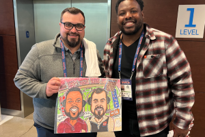 April 30, 2023 ~ Michigan Panthers play-by-play team Chris Renwick and Jehuu Caulcrick pose with a fan-drawn caricature drawing as they get set to call the Panthers / Generals game at Ford Field. Photo ~ Curtis Paul