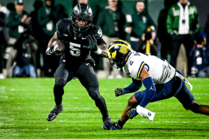 Oct. 21, 2023 ~ Michigan State's Nathan Carter runs the ball as Michigan's Will Johnson closes in during the first quarter at Spartan Stadium. Photo: Nick King ~ USA TODAY NETWORK