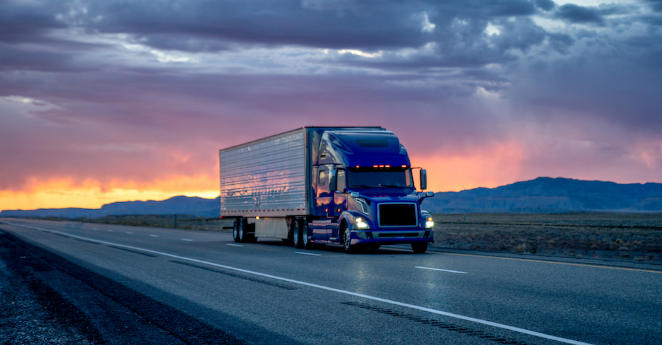 Heavy Hauler Semi-Trailer Tractor Truck Speeding Down a Four-Lane Highway with a Dramatic and Colorful Sunset or Sunrise In the Background