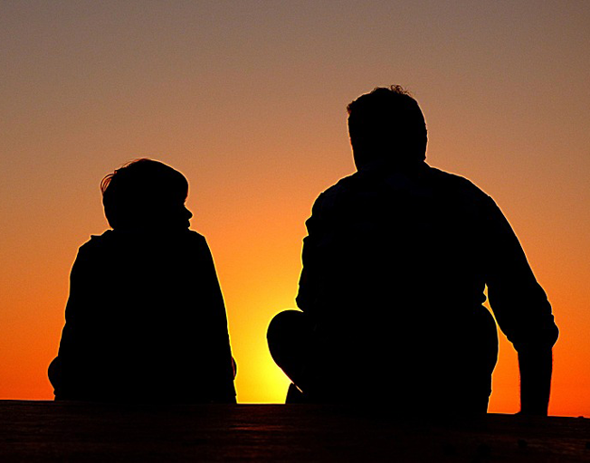 A child and dad silhouetted by sunset.