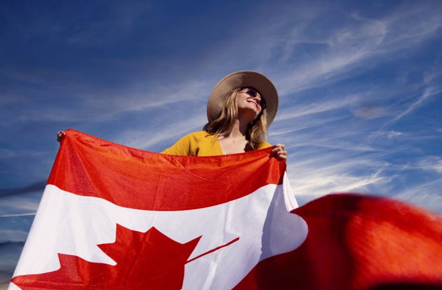 A joyful woman holding the Canadian flag under a clear blue sky, symbolizing national pride.