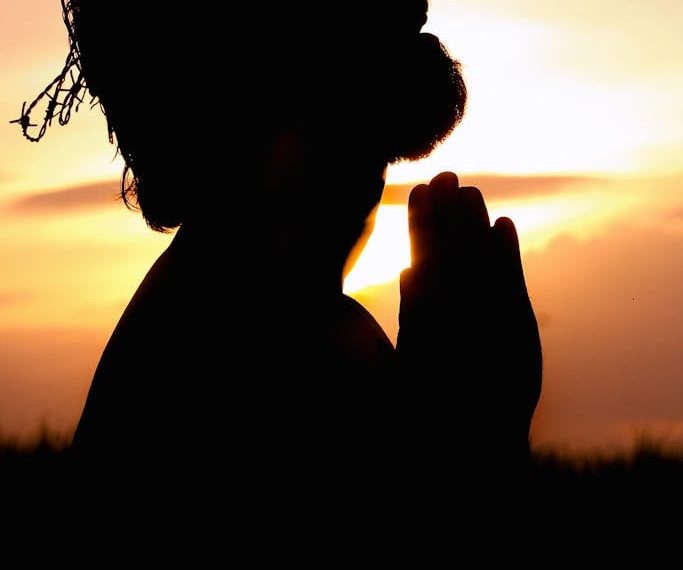 A silhouette of a man praying at sunset, wearing a crown of thorns, symbolizing faith and hope.