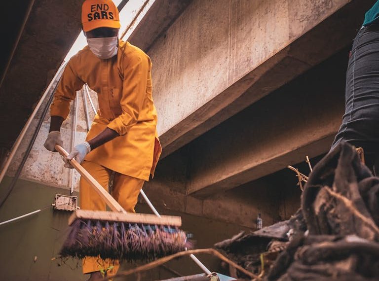 Man in Uniform Cleaning Dirt with Broom