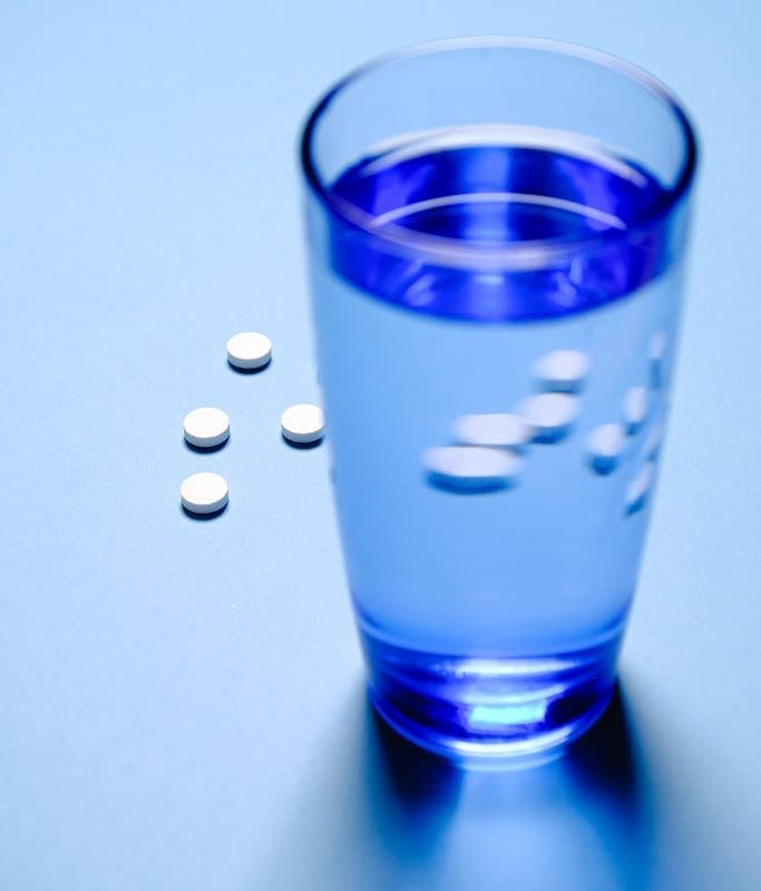 Blue Drinking Glass With Water and White Medicine Pills