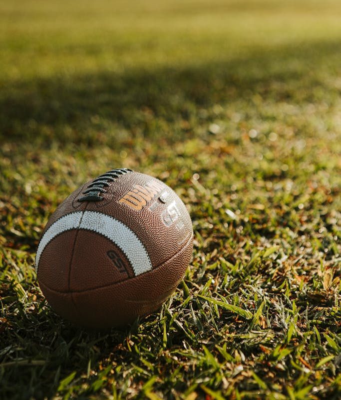 A football ball sits on the grass in the sun