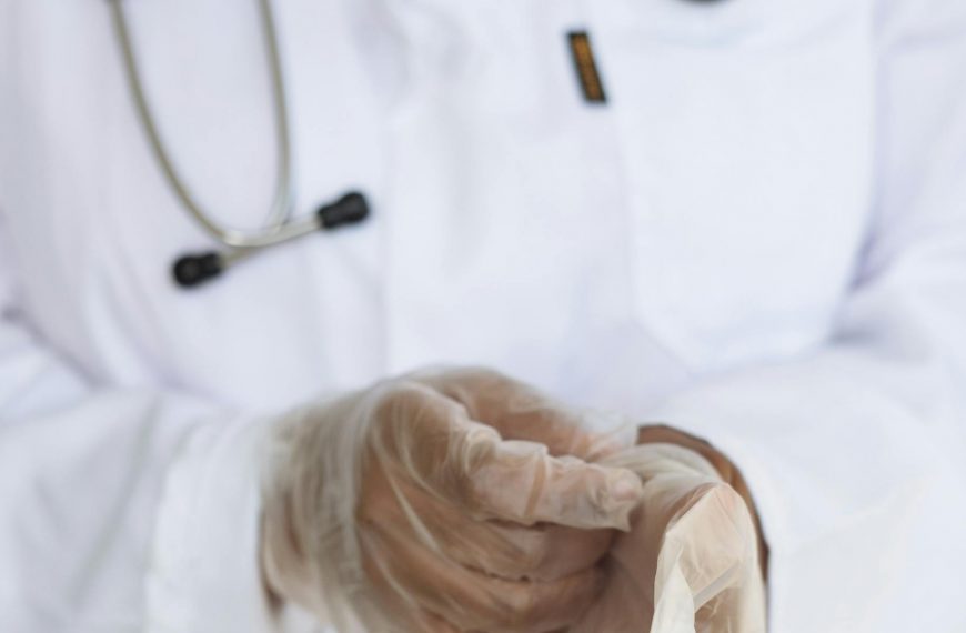 Faceless ethnic medical worker in lab coat and stethoscope taking of transparent gloves after approaching patients for examination in modern hospital